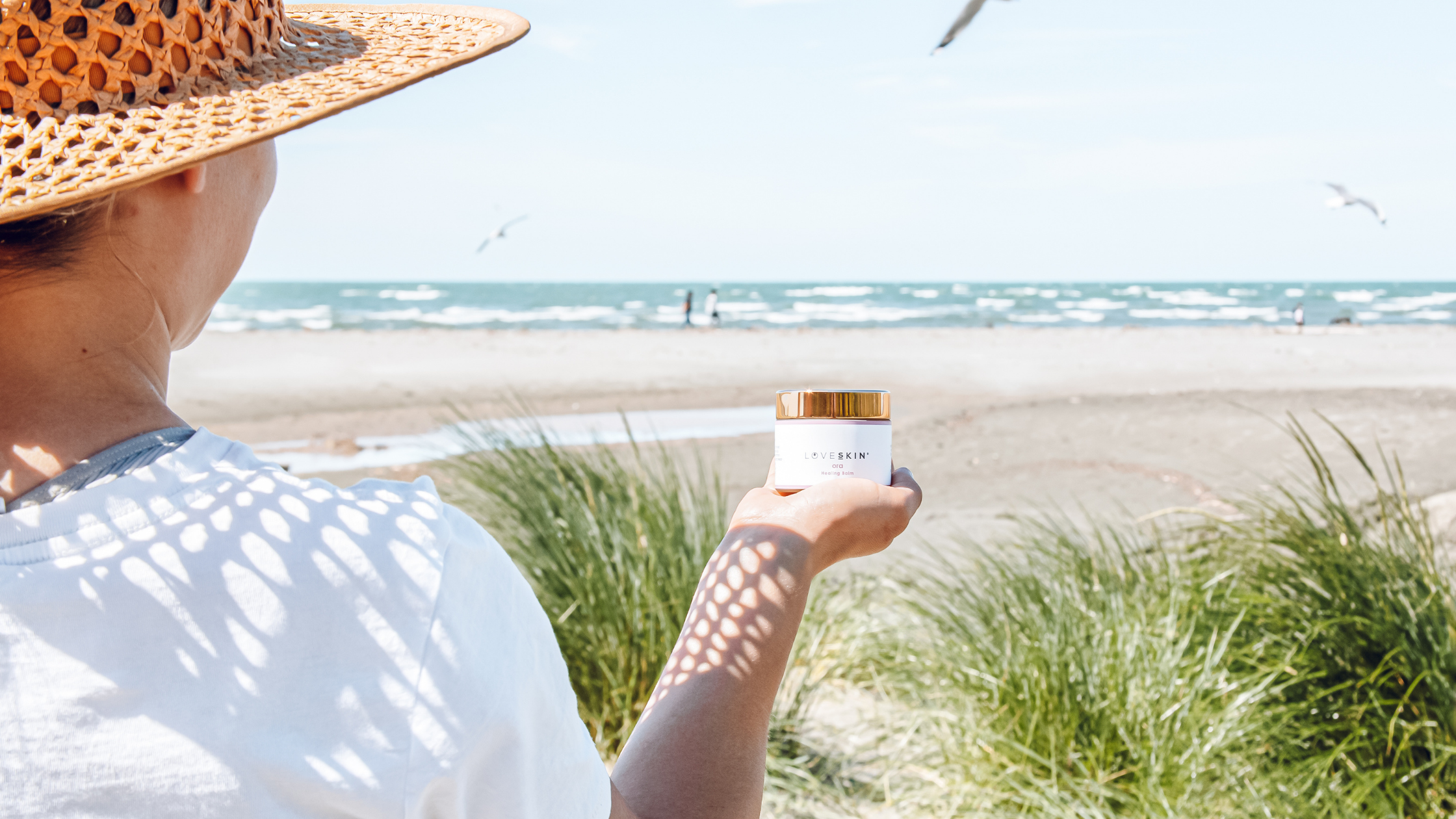 Woman holding ora balm for sensitive skin at the beach