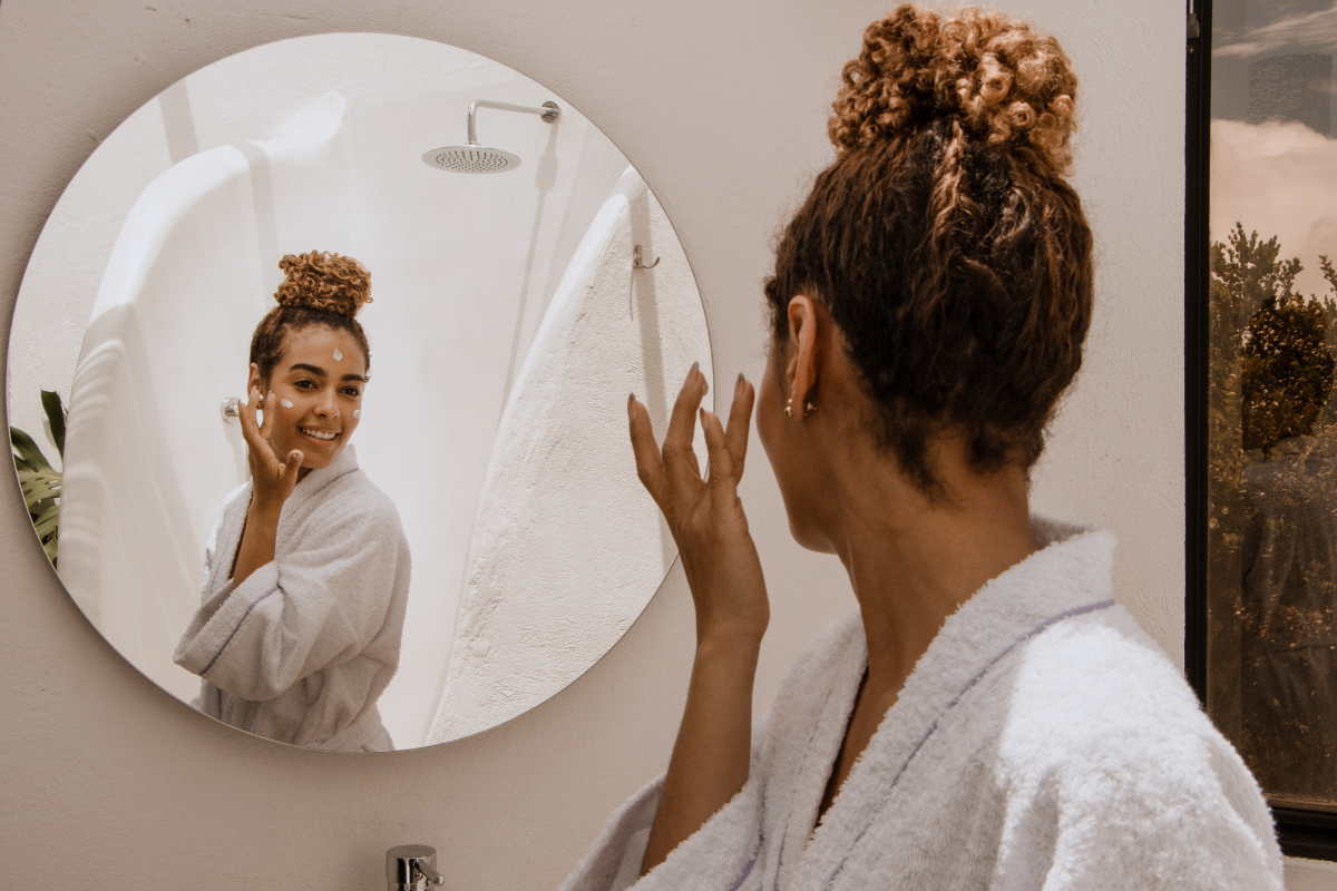 Woman applying skincare in front of mirror for fresh, glowing spring skin.