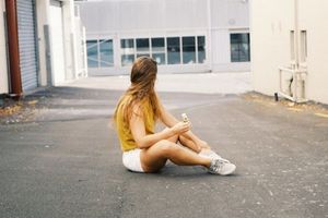 woman sitting casually on concrete looking away from camera holding bottle of kiri aroha serum