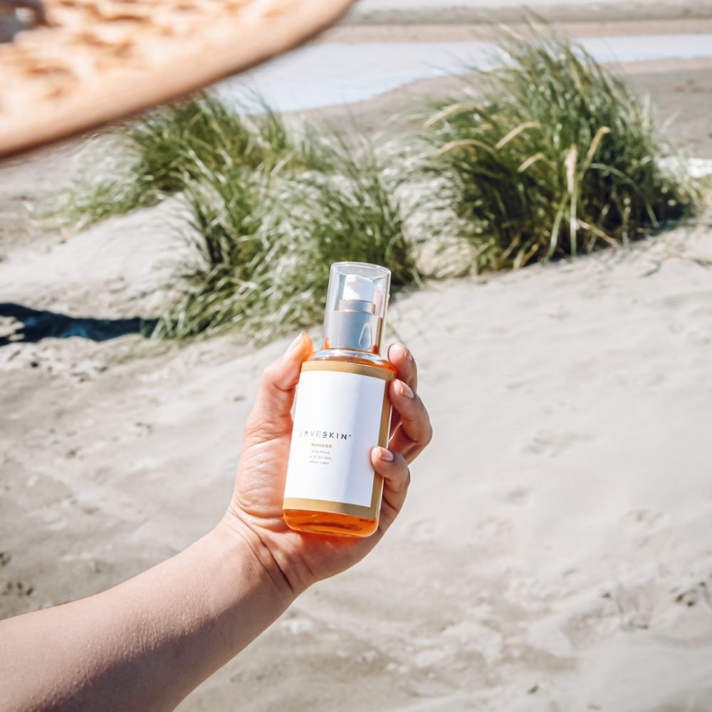 Hand holding a bottle of LOVESKIN's Mahana Body Oil product on a beach