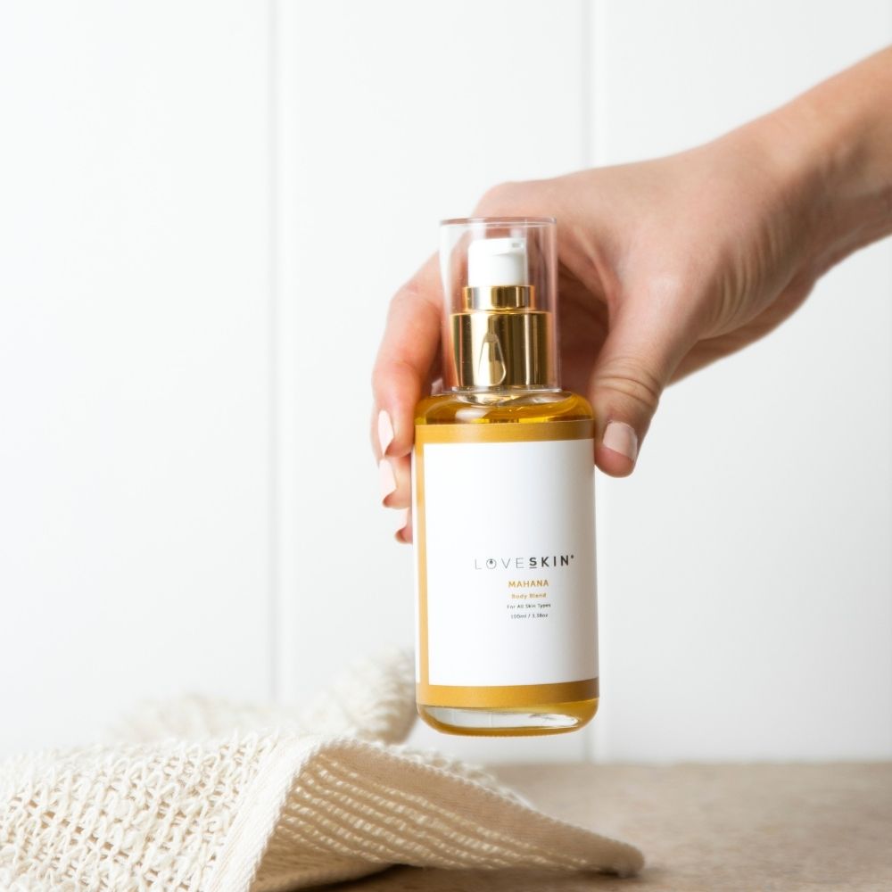 Hand holding a bottle of LOVESKIN's Mahana Body Oil skincare product against a neutral background