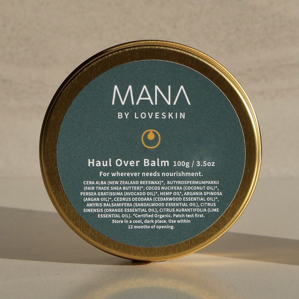 Tin of Mana by Loveskin Haul Over Balm with gold lid and green label on a beige background.