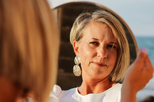 middle aged woman looking at her glowing skin in mirror