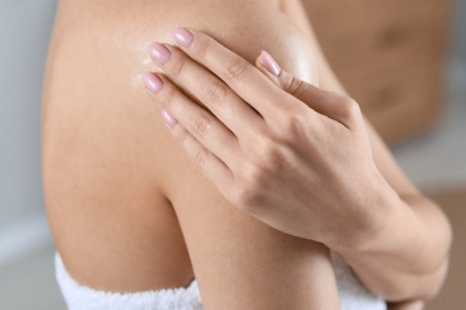 Woman rubbing in skincare oil to shoulder 