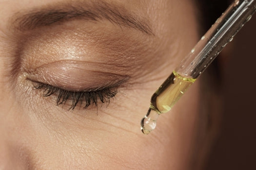 oil dropper held in front of close up of womans face with eye closed
