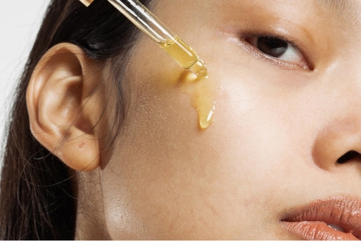 asian woman dropping natural skincare oil onto her cheek