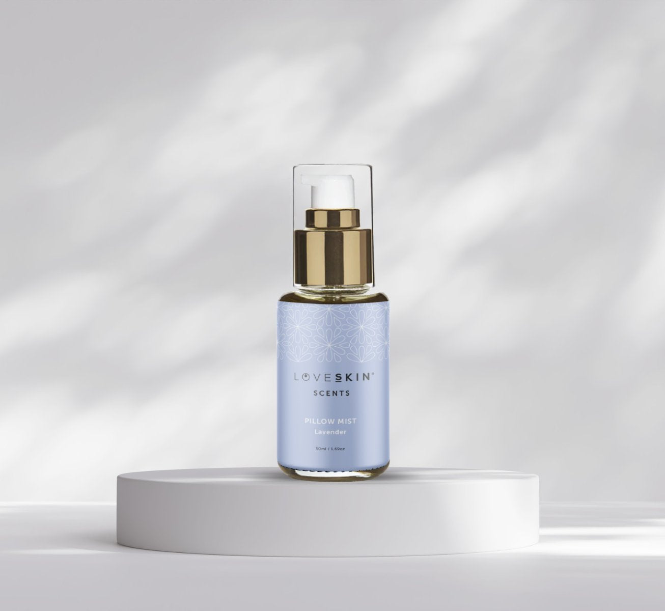 LoveSkin Scents Pillow Mist Lavender spray bottle with gold pump dispenser on white platform against soft grey background