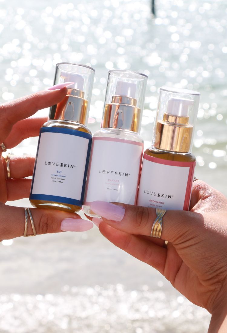 "Close-up of tanned hands holding 50ml LoveSkin Header 3-Step Skincare Ritual bottle against a sparkling sea backdrop."